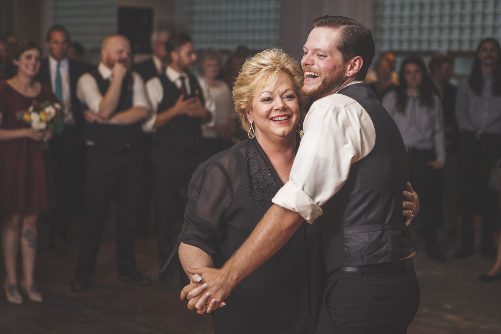 A woman and a man dancing and smiling, with people watching in the background at an event.
